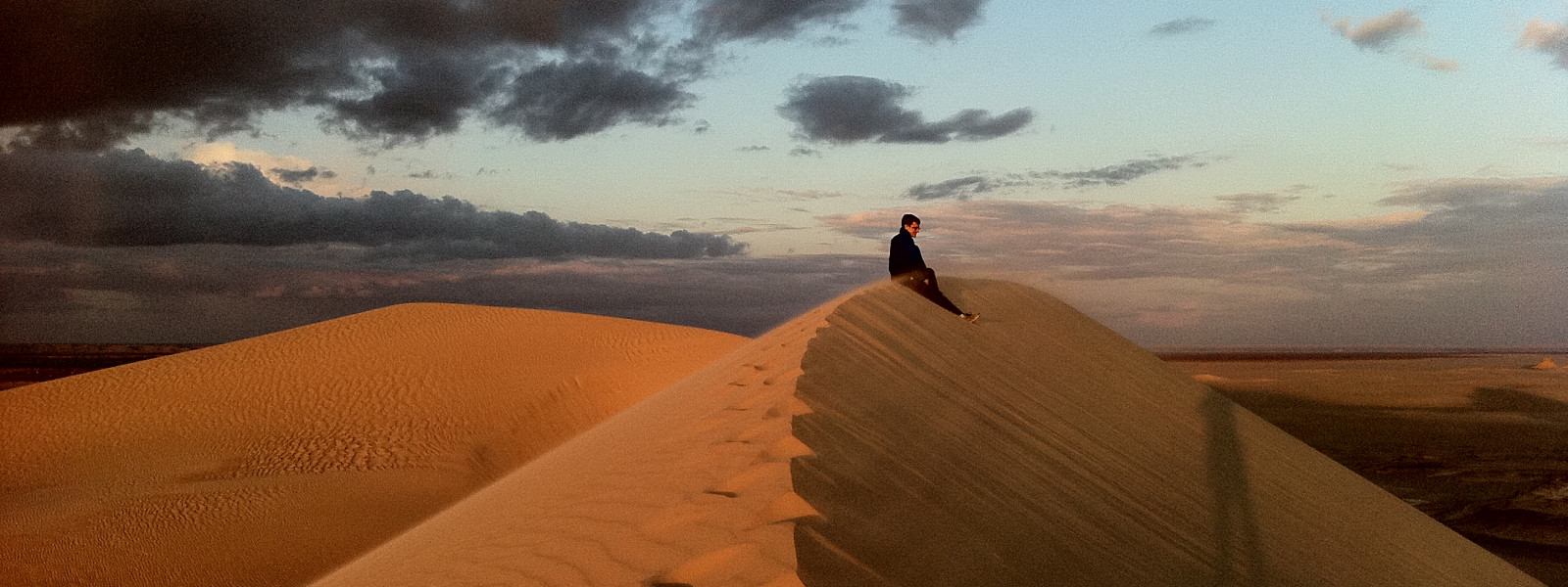 A solitary student sits atop a sand dune in the Sahara at sunset.