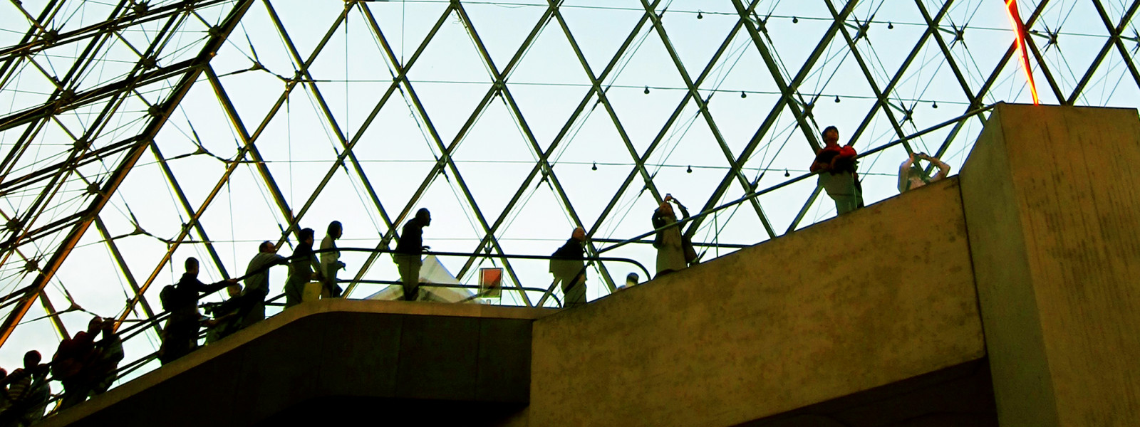 Visitors stand on the escalator inside of the Louvre Pyramid.