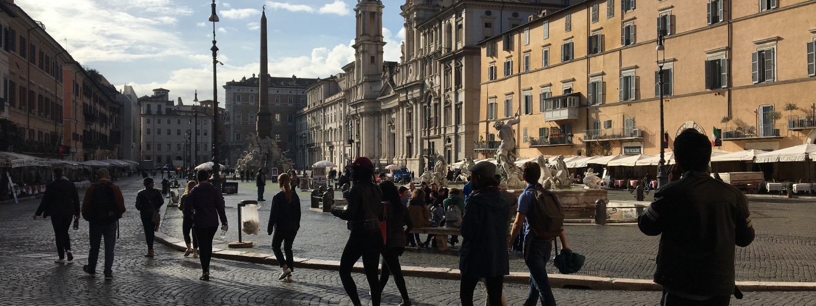 A line of students, in silhouette, walk through a public square in Rome.