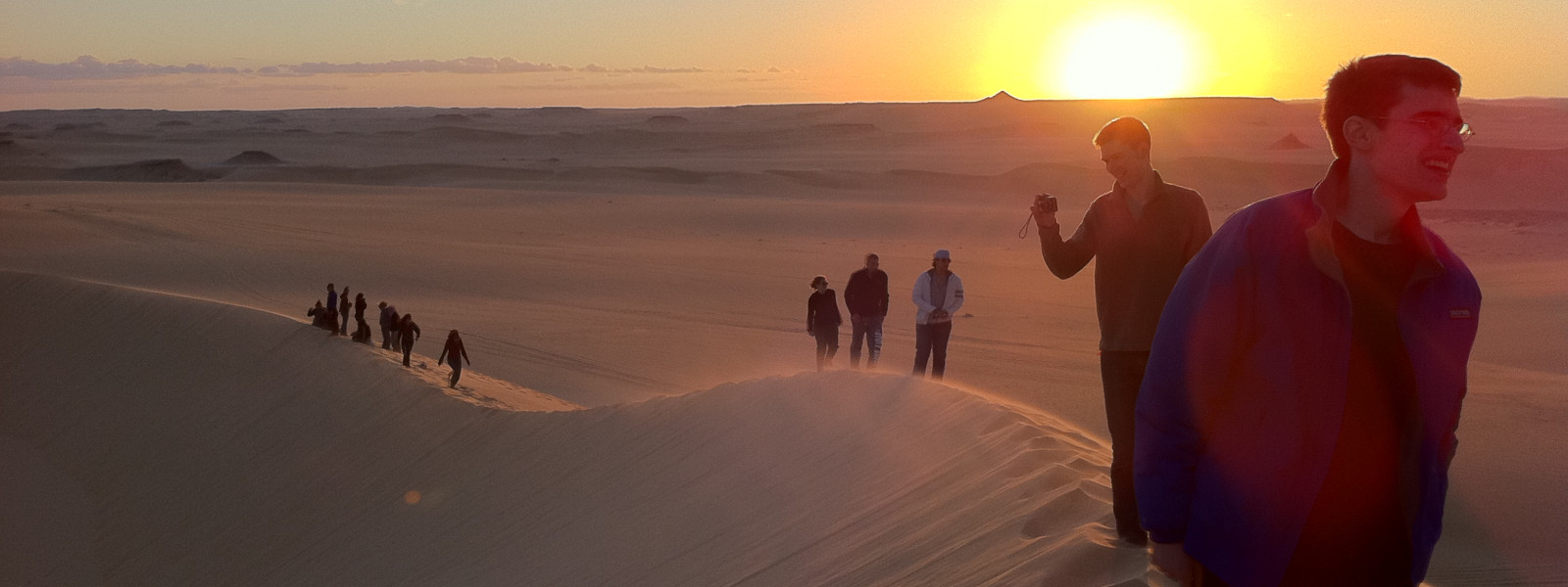 Students walk in a line on a sand dune as the sun goes down.