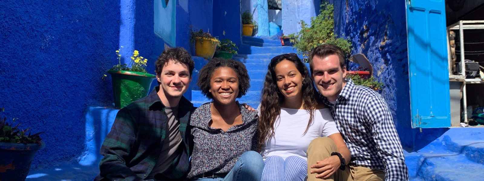 Four students pose for a photo while sitting close together on steps.