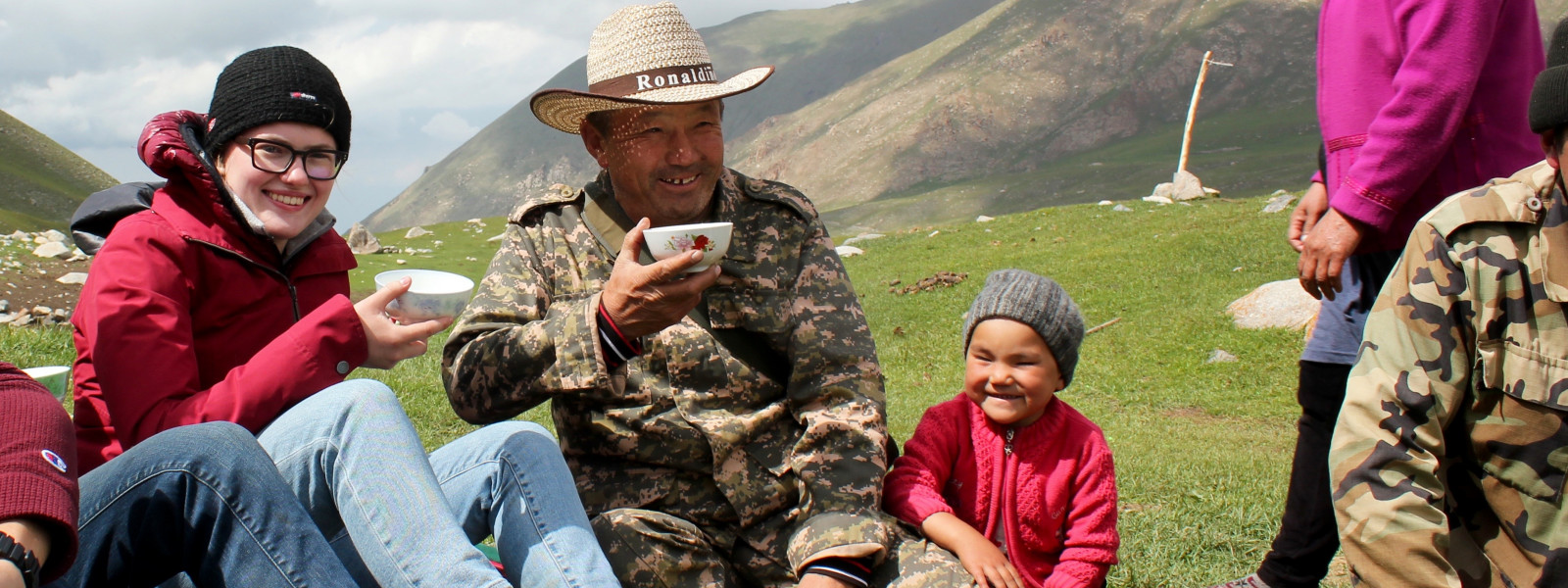 A student sits outside with a local family in Kyrgyzstan and enjoys a cup of sour milk.