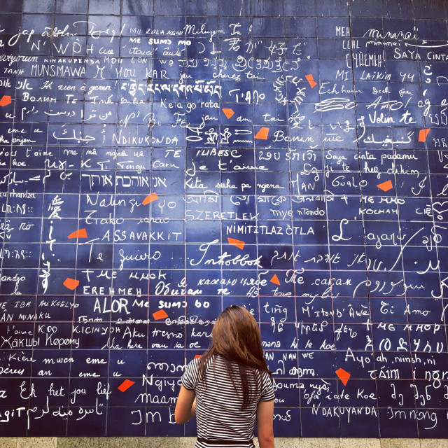 A student faces a tile wall that features the words “I love you” written in many different languages.