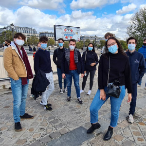 A group of students wearing face masks stand together by the bank of the Seine.