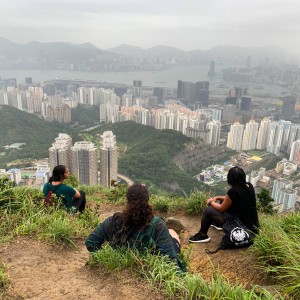 Three students sit and admire the view of buildings, water, and mountains.