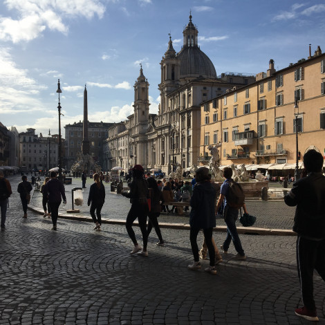 A line of students, in silhouette, walk through a public square in Rome.
