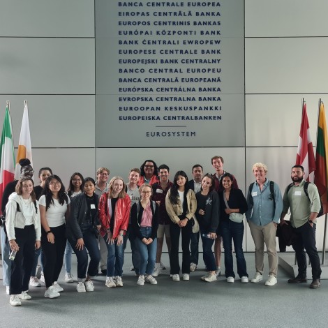 The group poses in front of a sign that lists European Central Bank in various languages. Country flags are displayed on either side.